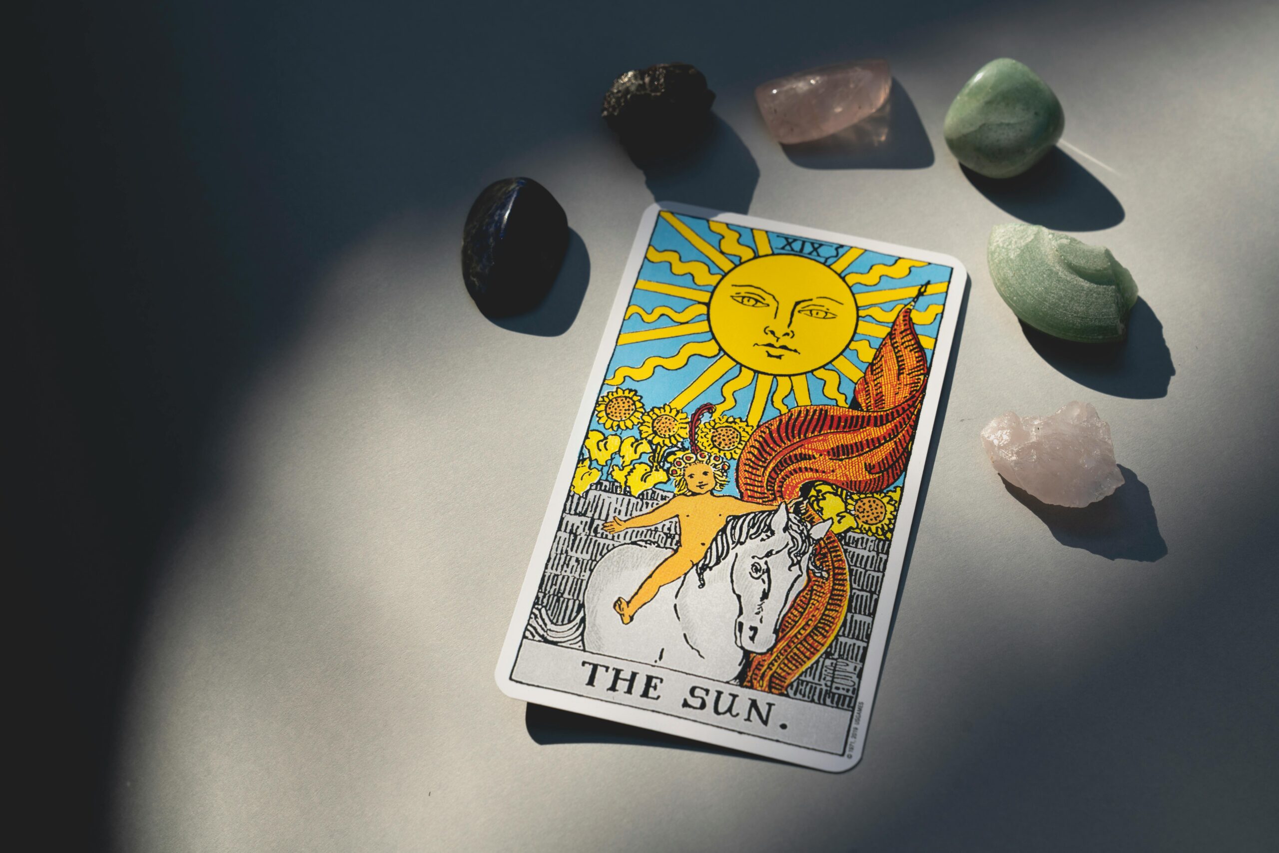 The Sun tarot card and crystals arranged on a surface with dramatic lighting and shadows.